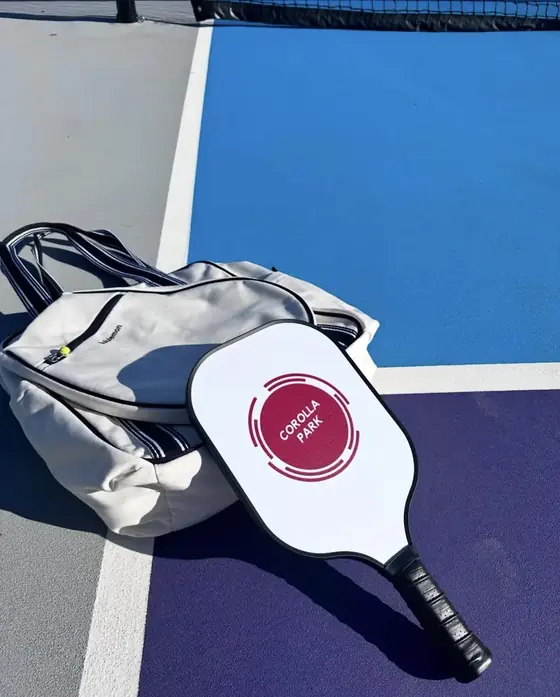 Custom white pickleball paddle with a Corolla Park circular logo