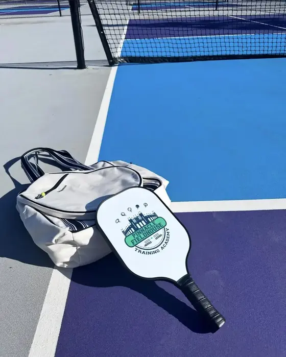 Custom white pickleball paddle with a training academy crest, on court