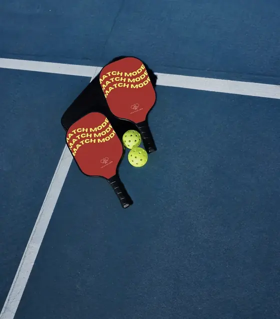Two red Match Mode pickleball paddles with a cover and two balls on a court