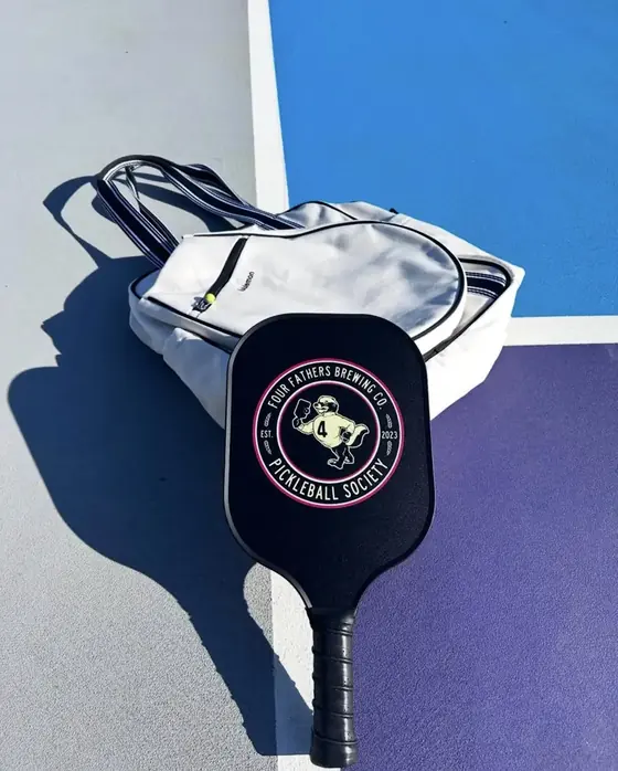 Black Four Fathers Brewing pickleball society paddle on a white court tote